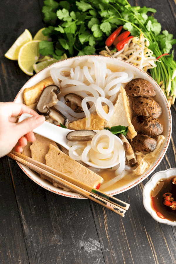 Banh canh chay in a bowl with a hand holding a spoon and chopsticks
