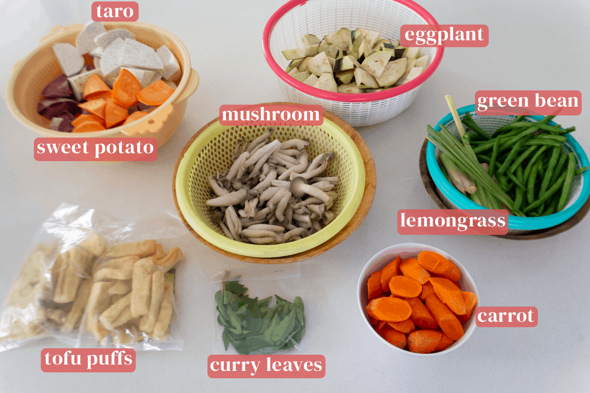 Colanders of sweet potato and taro chunks, eggplant pieces, lemongrass segments, mushroom and green beans along with a bowl of sliced carrots and bags of tofu puffs and curry leaves.