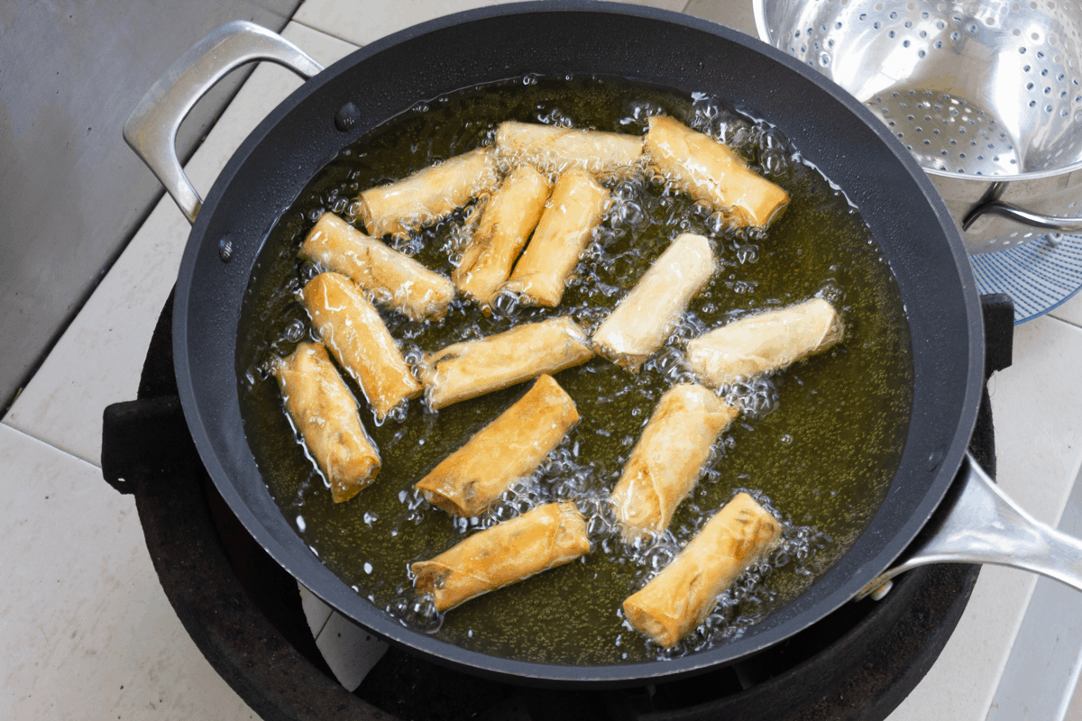 Spring rolls frying in a pan of oil.