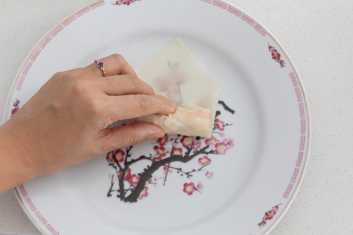 A hand rolling a spring roll up on a plate.
